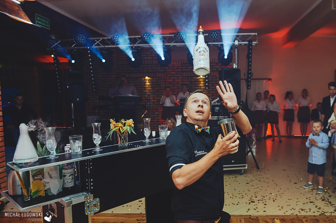 Barman żongluje butelką i shakerem na tle sceny z efektami świetlnymi