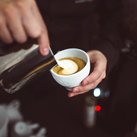 Barista nalewający mleko do filiżanki espresso, tworząc wzór latte art
