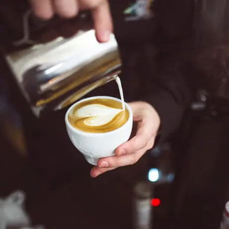 Barista tworzy wzór latte art, wlewając mleko do kawy w białej filiżance