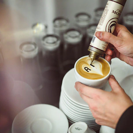 Ręka dekorująca kawę latte art za pomocą syropu