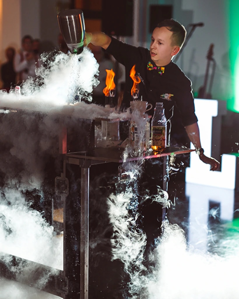 Barman wykonuje efektowny pokaz z dymem i płomieniami przy stole barowym