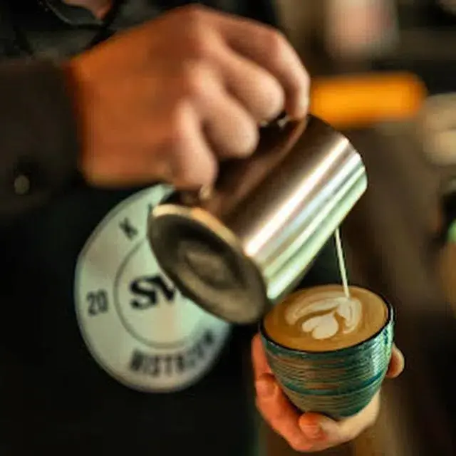Barista nalewający spienione mleko do filiżanki, tworząc wzór latte art