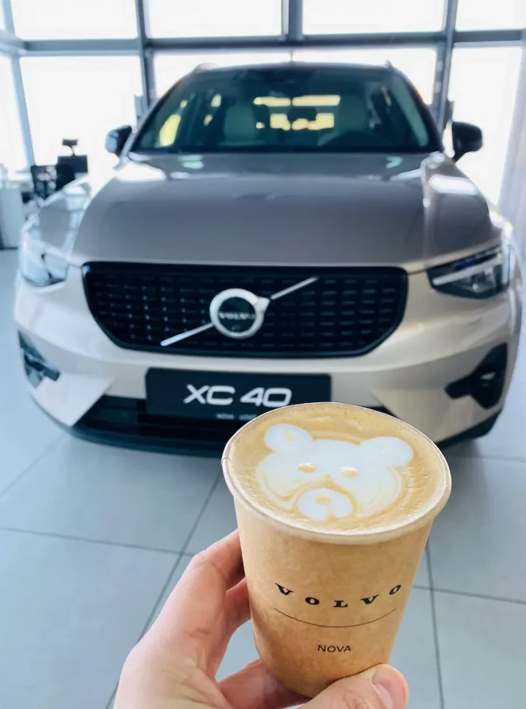 Kubek kawy z latte artem w kształcie misia, trzymany przed samochodem w salonie