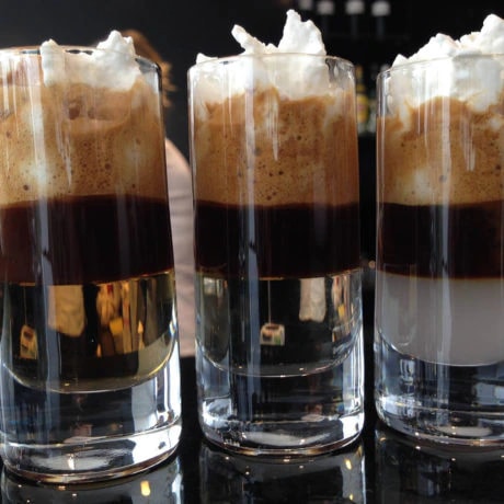 Trzy szklanki espresso z warstwami mleka, kawy i bitej śmietany