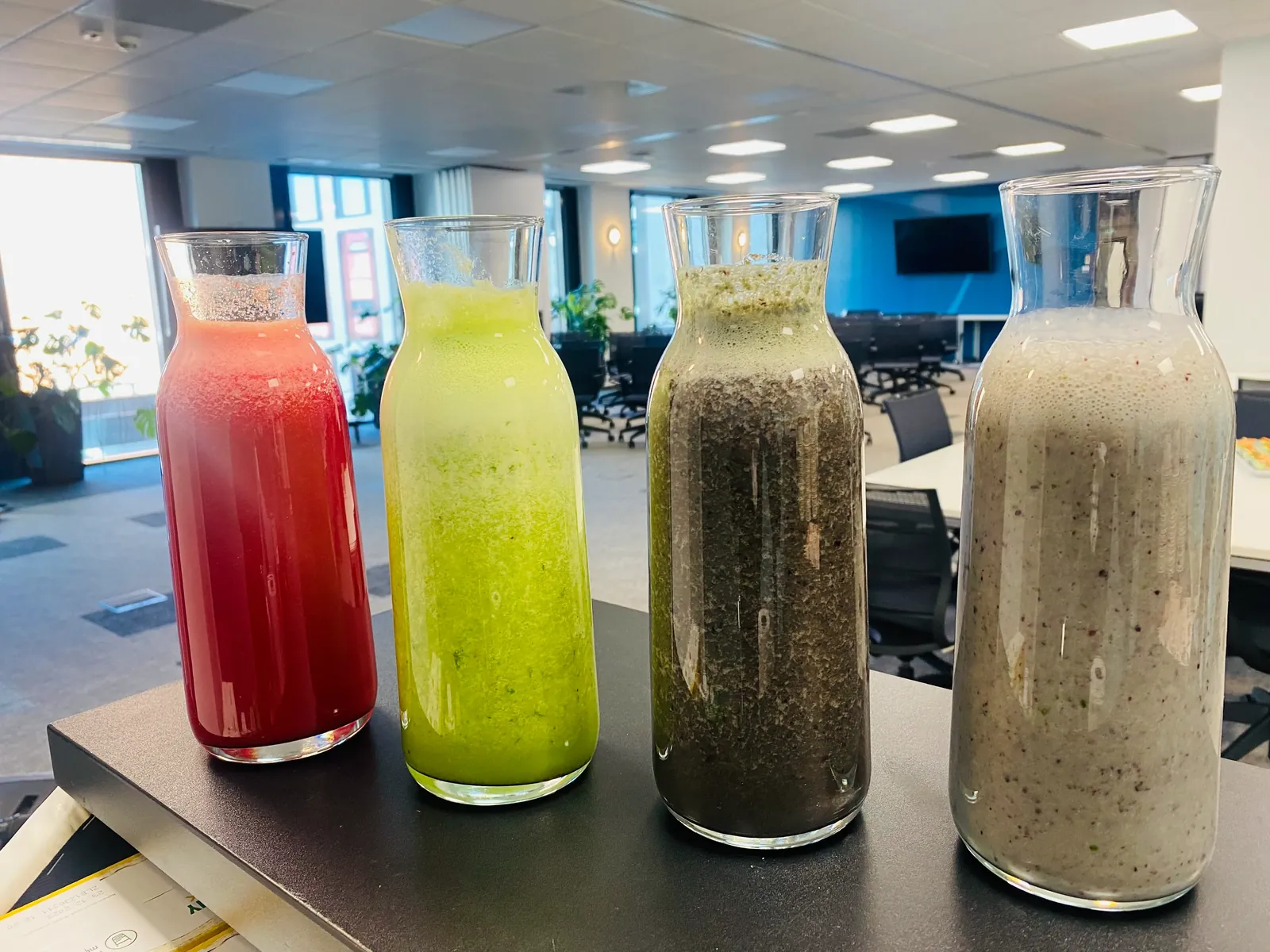 Cztery karafki ze smoothie w różnych kolorach na stole w biurze
