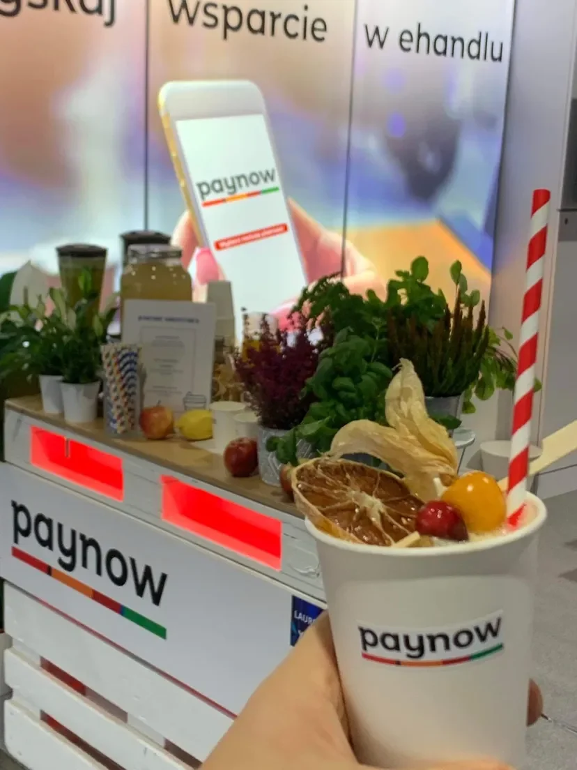 Kubek smoothie z suszoną pomarańczą w dłoni gościa przy stoisku Paynow