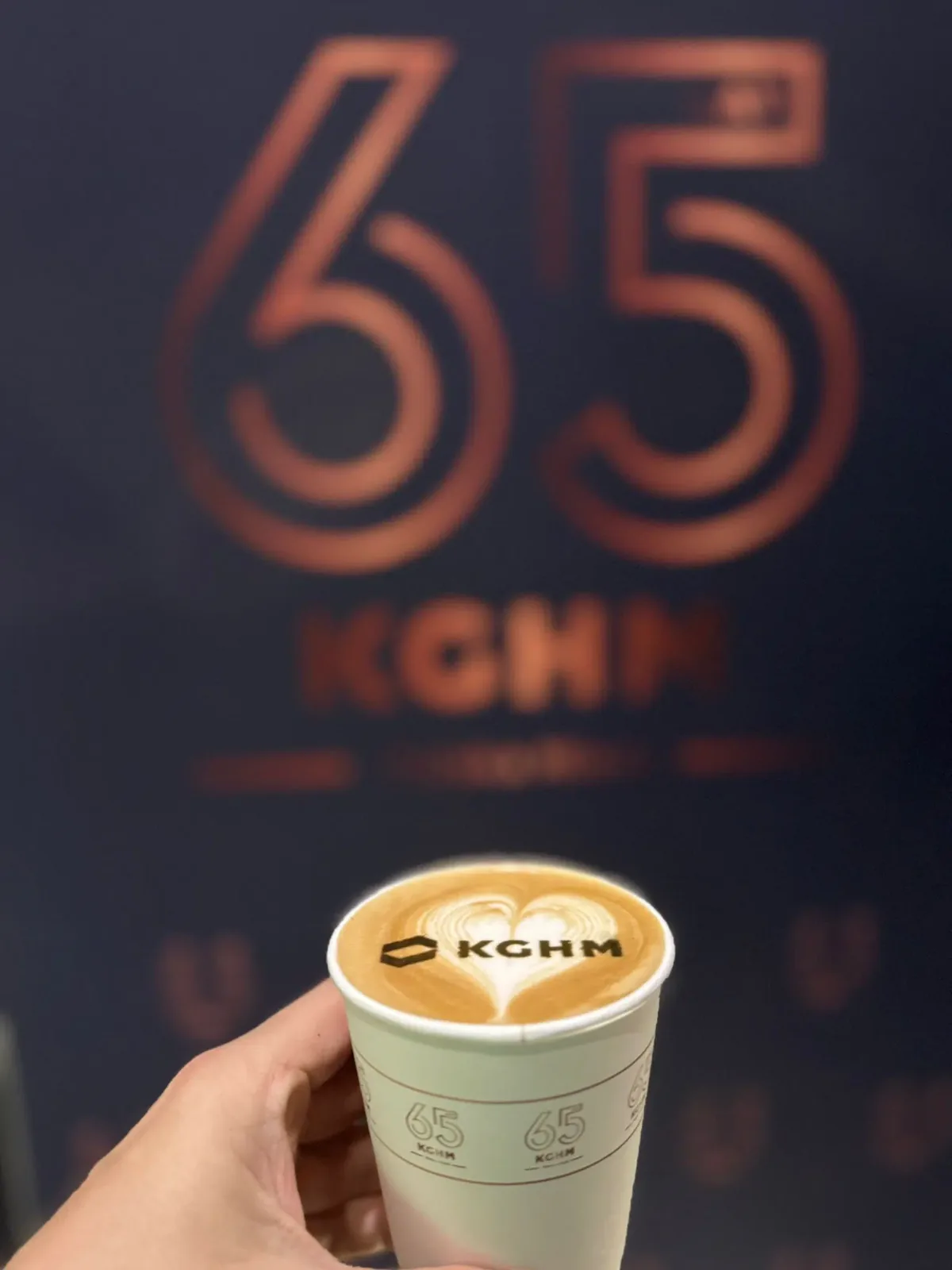 Kubek z logo KGHM na piance, w tle grafika sześćdziesiątej piątej rocznicy