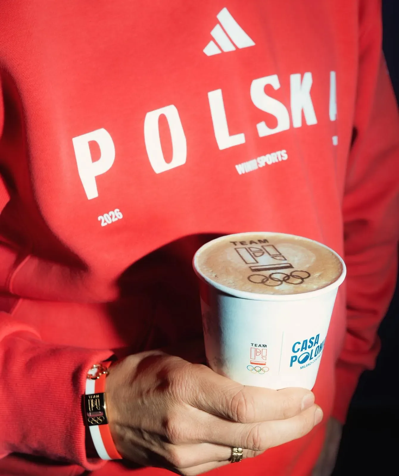 Kubek z logo olimpijskim trzymany przez osobę w bluzie reprezentacji Polski