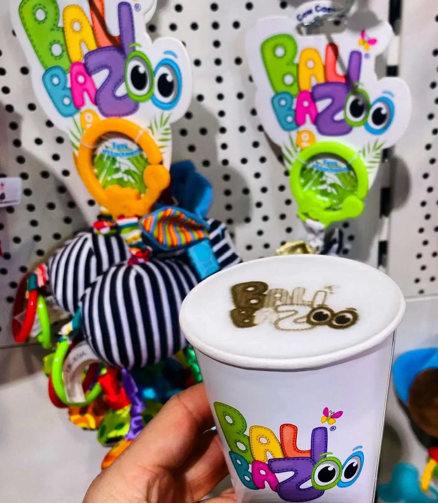 Kubek z logo Bali Bazoo na piance, w tle stoisko z zabawkami