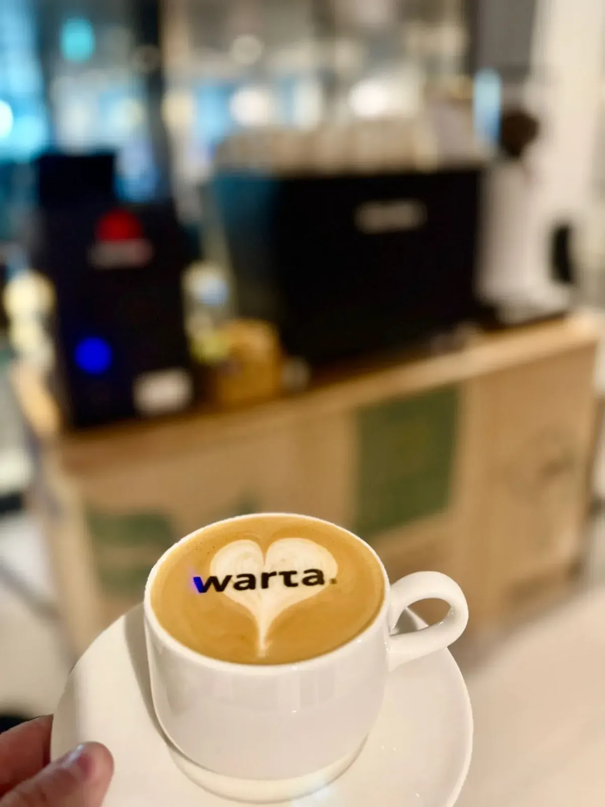 Filiżanka z logo Warty na piance, w tle stanowisko baristy