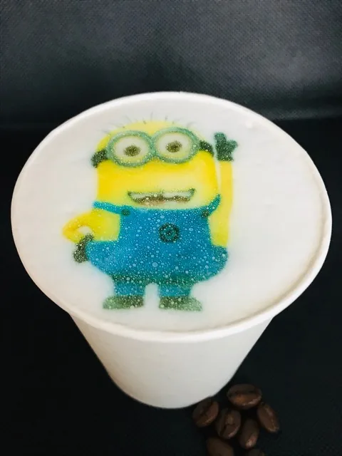 Kubek z wydrukiem minionka na mlecznej piance, obok ziarna kawy