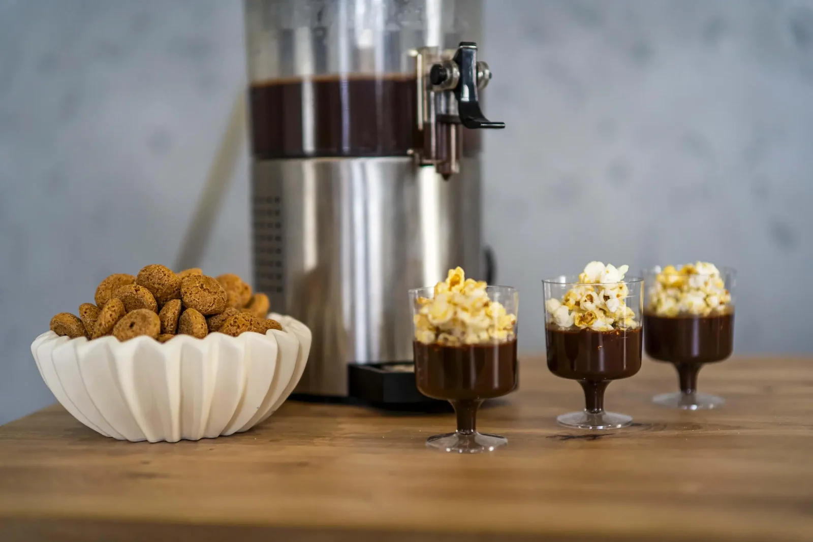 Dyspenser gorącej czekolady, miska z ciasteczkami i pucharki z popcornem na drewnianym blacie