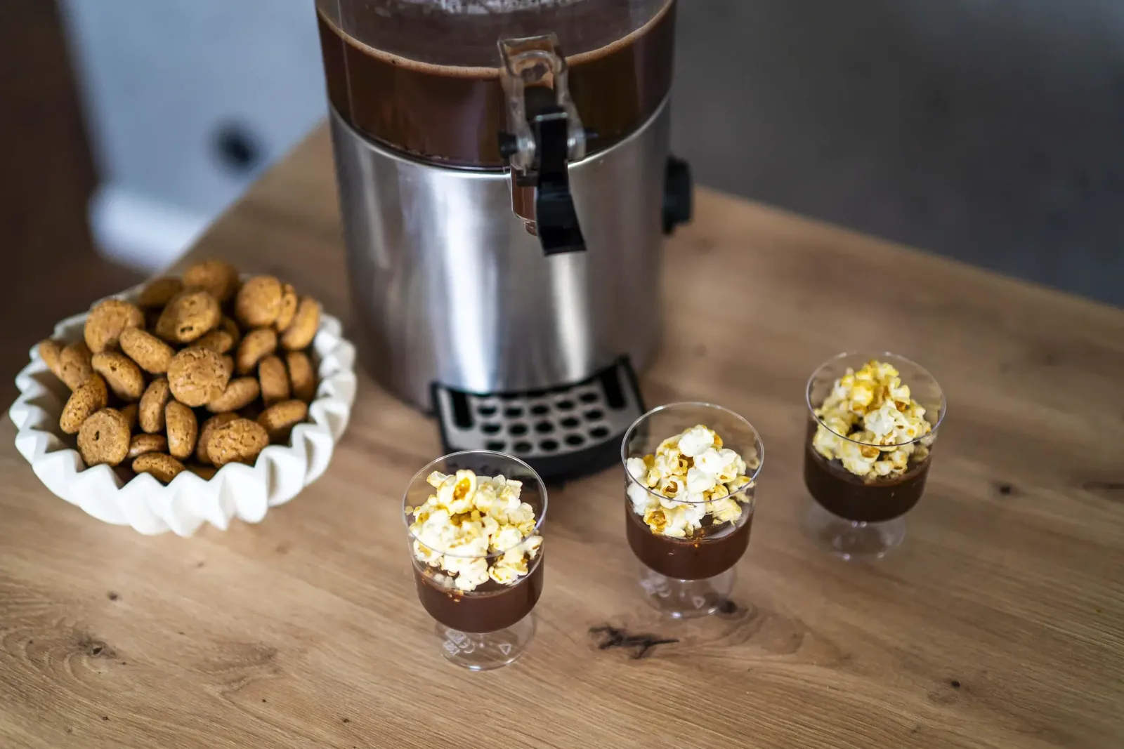 Kieliszki gorącej czekolady z popcornem widziane z góry, obok misa ciastek amaretti
