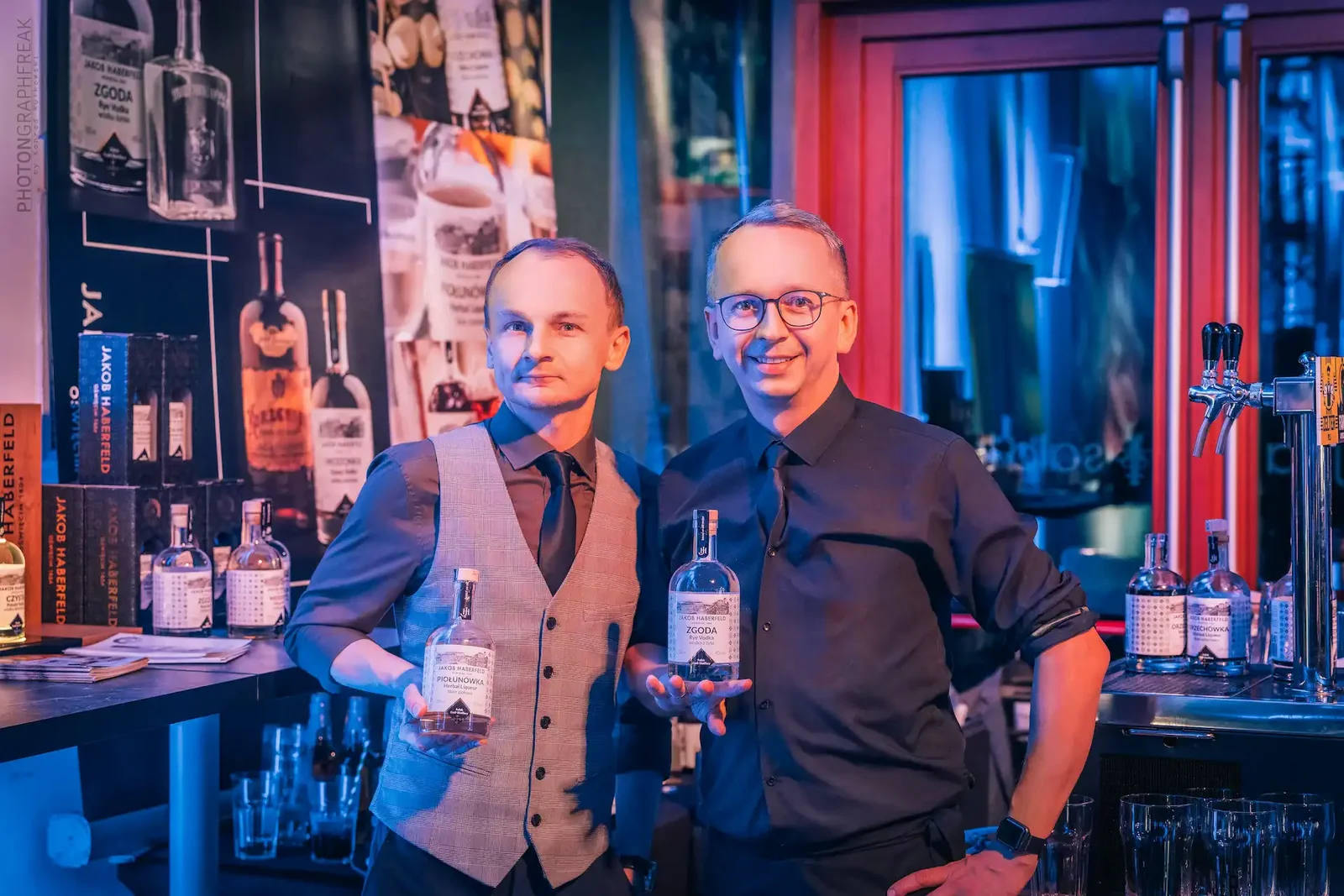 Dwaj prowadzący degustację z butelkami wódki przy barze w kolorowym świetle