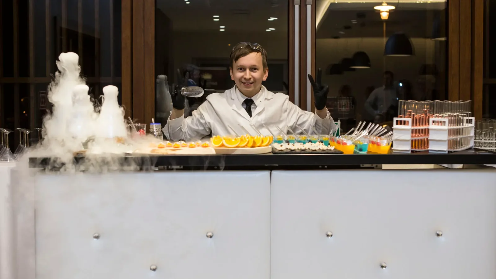 Barman w białym kitlu za barem molekularnym, obok dymiące kolby z ciekłym azotem