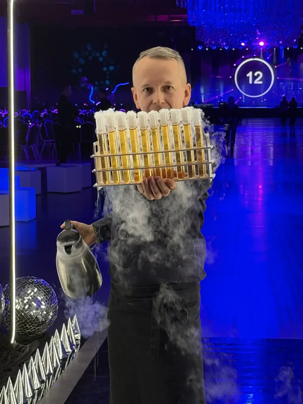 Barman niesie tacę z probówkami, spod niej unosi się dym z ciekłego azotu