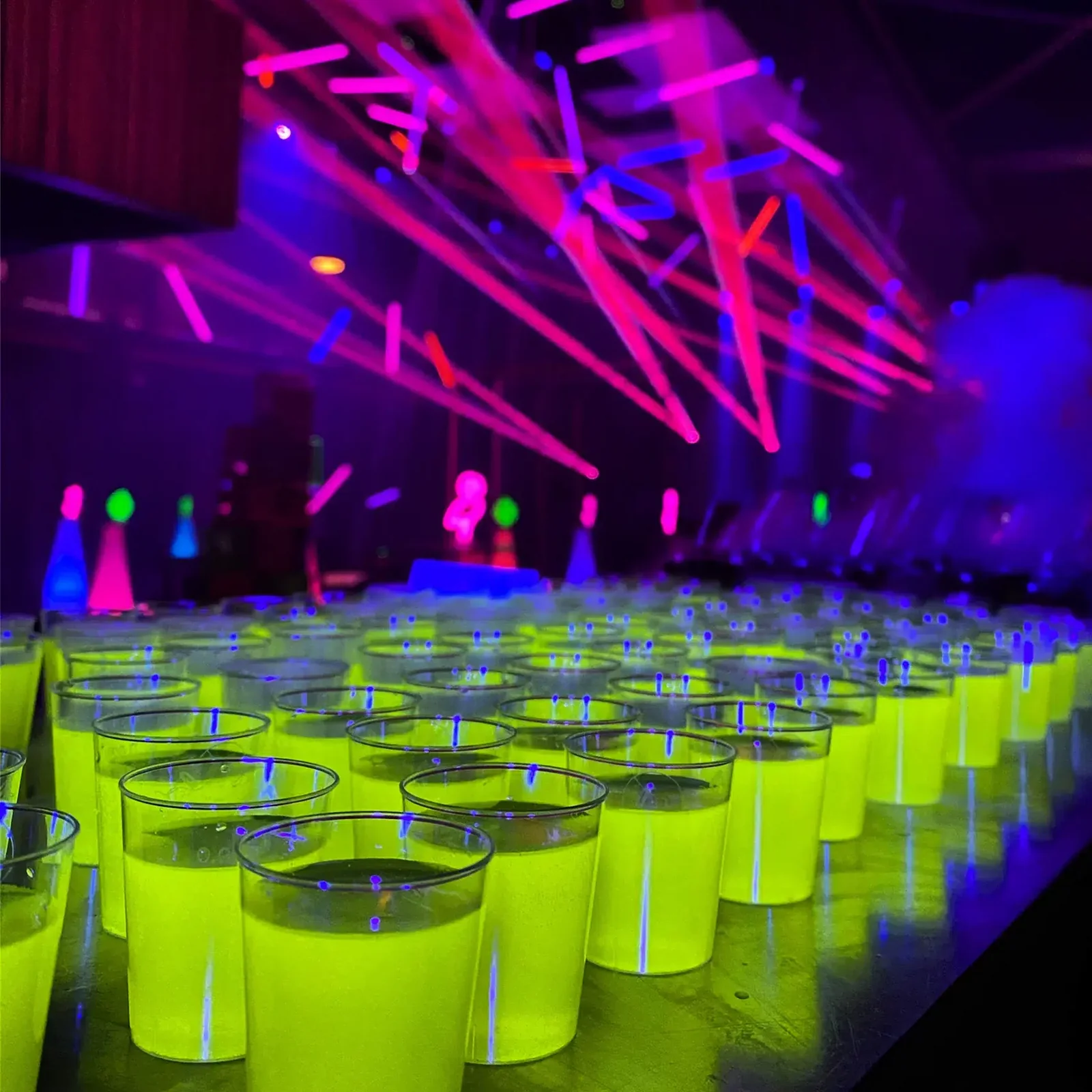 Rzędy świecących fluo shotów na barze, w tle lasery i światła sceniczne
