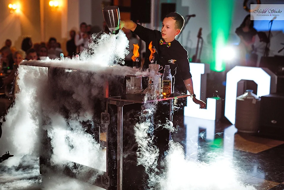 Barman wylewa ciekły azot na bar podczas wesela, obok płonące butelki