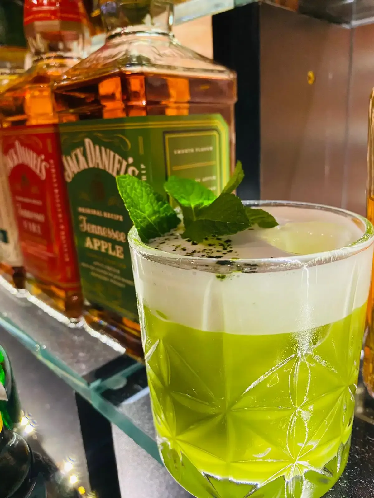 Zielony koktajl z pianką przed butelkami whiskey na barze