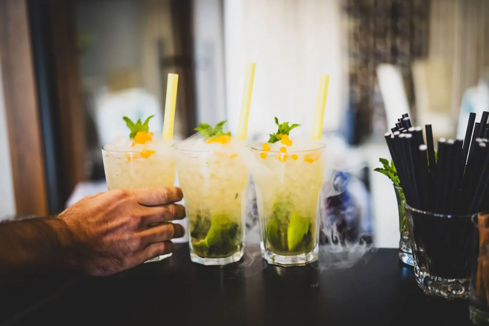 Barman podaje trzy szklanki mojito ze słomkami
