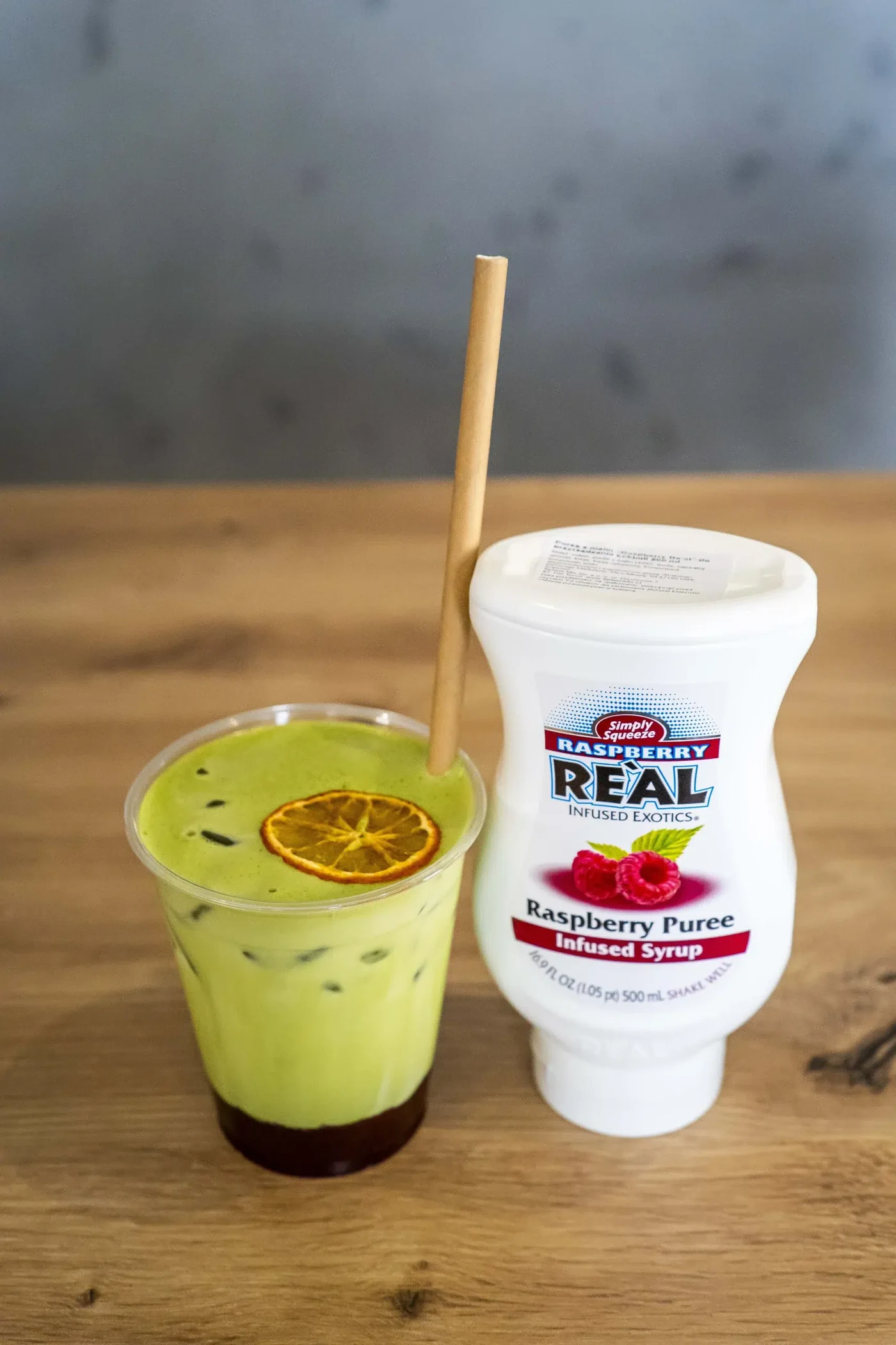 Mrożona matcha z suszoną cytryną w kubku obok butelki syropu malinowego