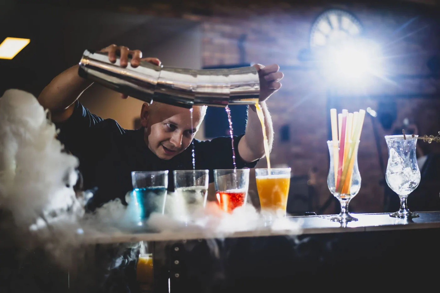 Barman nalewa kolorowe drinki z dużego shakera do szklanek
