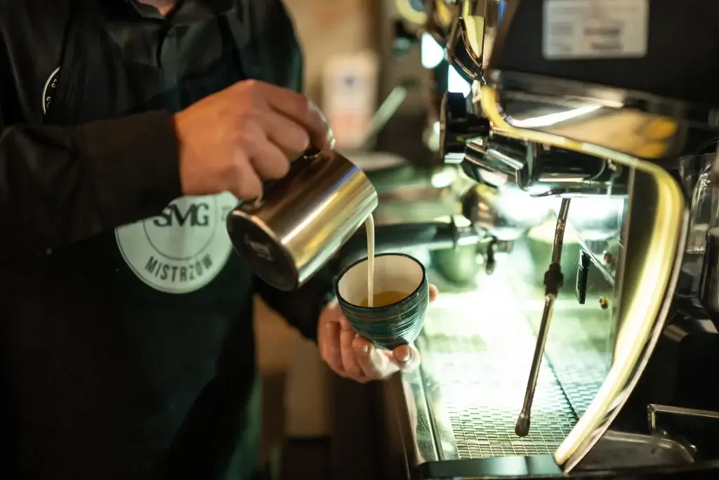 Barista nalewający spienione mleko do filiżanki przy ekspresie do kawy